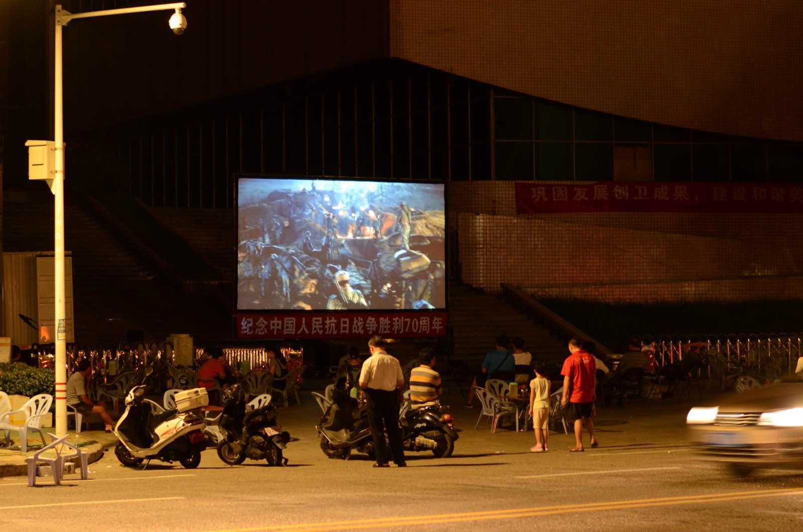 广场不远的露天电影放映着抗战影片,茶客们三三两两的看着. 小公园